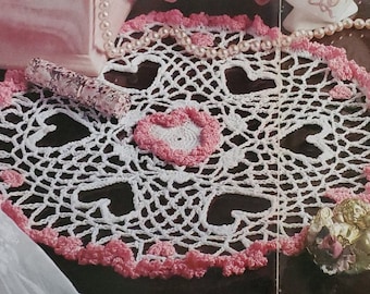 Peut inclure: Napperon en crochet blanc avec une bordure en crochet rose et six cœurs roses au centre.