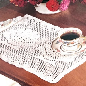 May include: White crocheted doily with a floral design, a cup of coffee and a silver spoon on a wooden table.