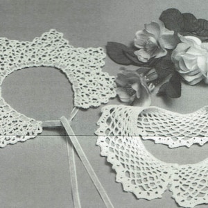 May include: Two white crocheted collars, one with a more intricate design than the other, are displayed on a grey background. A bouquet of white flowers is placed behind the collars.