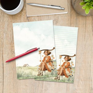 May include: Two sheets of stationery paper featuring a watercolor illustration of a person with brown hair wearing an orange and white dress, sitting on a wooden swing decorated with white daisies in a grassy field with a small house in the distance.
