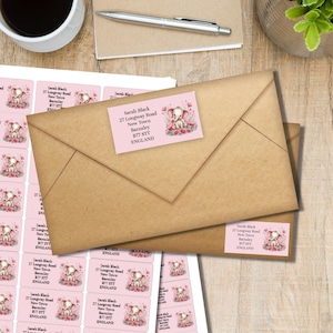 May include: Kraft paper envelopes with address labels featuring a pink elephant illustration. The labels include the name "Sarah Black", address, and the word "ENGLAND". A cup of coffee and a pen are in the background.