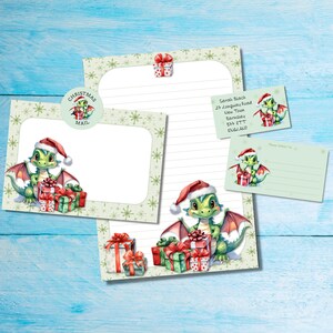 May include: A stationery set featuring a Christmas theme. The set includes a lined letter sheet, a blank card, an envelope, and a small gift tag. Each item has a green dragon wearing a Santa hat and holding gifts. The set is decorated with snowflakes.