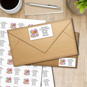 May include: A rectangular white address label featuring the colorful text "do all THINGS WITH KINDNESS" alongside a printed name and address. The label is shown applied to a brown paper envelope, with a full sheet of identical labels visible underneath.