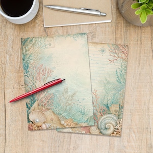 Könnte beinhalten: Zwei Briefpapierbögen mit einem Unterwassermotiv im Vintage-Stil, bestehend aus Korallen, Muscheln und Perlen in Blau- und Beigetönen. Ein Bogen ist unliniert, der andere hat blaue horizontale Linien und eine Kompassrosengrafik am oberen Rand.