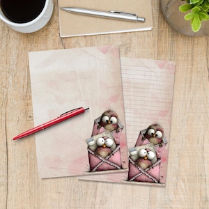 Può includere: Due fogli di carta da lettere con un design rosa e bianco, con gufi dei cartoni animati che sbucano da buste rosa. Una penna rossa poggia a sinistra, con una tazza di caffè e una penna sullo sfondo. La carta da lettere è a righe e non a righe.