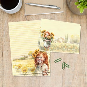 Op de afbeelding: Briefpapier set met een aquarel illustratie van een jong meisje met rood haar dat zonnebloemen in een veld vasthoudt. De set bevat gelijnd papier en kaarten met hetzelfde ontwerp, dat een zonnig, pastoraal thema oproept.