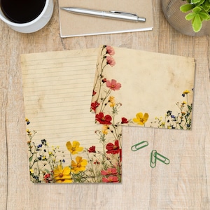 May include: A set of stationery featuring a lined sheet and a blank card, both with a vintage beige paper texture and a decorative border of colourful wildflowers including red, yellow, and blue blossoms, accompanied by three green paper clips.