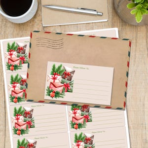 Könnte beinhalten: Ein Briefpapier-Set mit einem großen braunen Umschlag mit rot-weiß-blauen Bordüren und einem kleineren Adressetikett. Das Etikett und der Umschlag sind mit Aquarellillustrationen von verpackten Geschenken und Grünzeug verziert. Ein Stift und eine Kaffeetasse sind ebenfalls sichtbar.
