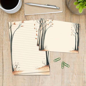 Op de afbeelding: Een crèmekleurige briefpapierset met een bosthema, donkere boomstammen en verspreide oranje herfstbladeren. De set bevat een gelinieerd vel papier, een bijpassende ongelinieerde kaart en drie groene paperclips.