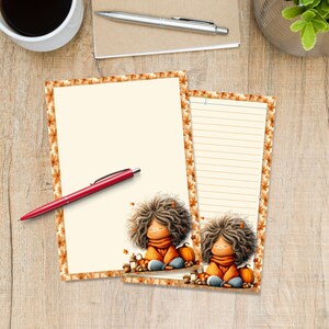 May include: Two sheets of stationery paper featuring a border of orange and brown autumn leaves. Each sheet displays a cartoon character with voluminous brown hair, wearing an orange scarf, sitting beside a pumpkin. One sheet is blank, one is lined.
