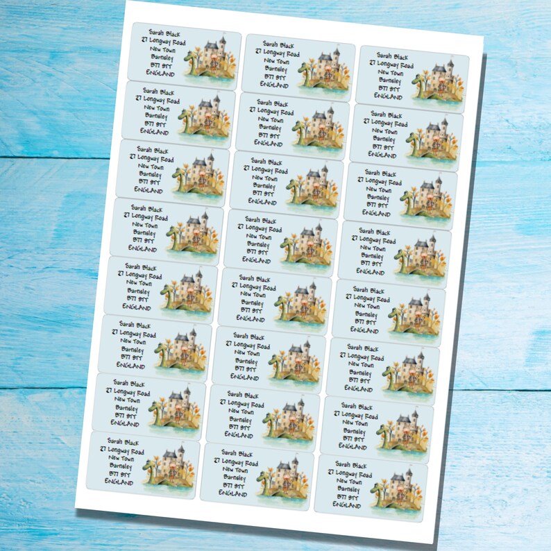 Puede incluir: Una hoja de 20 etiquetas de direcci&oacute;n personalizadas con una ilustraci&oacute;n caprichosa de un castillo, un drag&oacute;n y hojas de oto&ntilde;o. Las etiquetas son blancas con un fondo azul claro y el texto "Sarah Black, 27 Longway Road, New Town, Barnsley, England" est&aacute; impreso en negro.