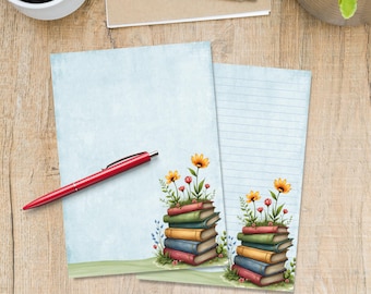 May include: Two sheets of stationery with a light blue background. One sheet is lined, the other is blank. Both feature a stack of colorful books with flowers growing from the top. A red pen rests on the blank sheet.