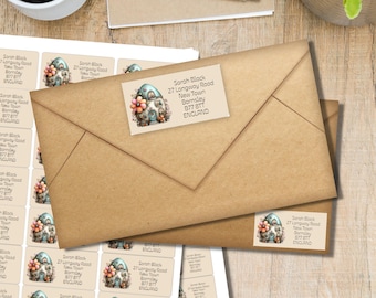 May include: A stack of address labels and a brown envelope. The labels feature a whimsical illustration of a small house with flowers and the text "Sarah Black, 27 Longway Road, New Town, Barnsley, 877 8TT, ENGLAND."