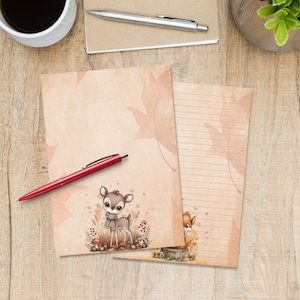 Puede incluir: Dos hojas de papel de carta con fondo color canela claro y un patrón sutil de hojas de otoño. Una hoja está en blanco y la otra tiene líneas horizontales. Ambas muestran una pequeña ilustración de un cervatillo con bufanda en la esquina.