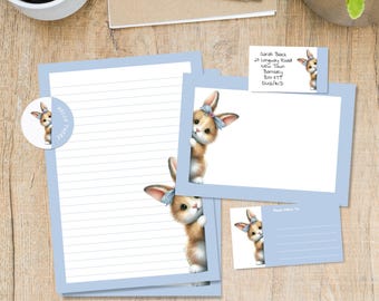 May include: Stationery set featuring a cute bunny illustration with a blue bow. The set includes lined paper, a blank card, a postcard, and a business card, all with a light blue border. A sticker with the text "Hello There" is also included.