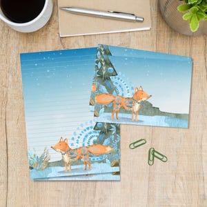 Op de afbeelding: Briefpapier set met een aquarel illustratie van een vos met ingewikkelde patronen. De vos staat in een besneeuwd landschap met een blauw-wit kleurenschema. De set bevat gelijnd papier en kaarten, perfect voor het schrijven van brieven.