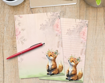 May include: Two sheets of stationery paper featuring a soft pink background with a floral border and a small fox wearing a flower crown. One sheet is blank, and the other has horizontal lines for writing. A red pen rests across the blank sheet.