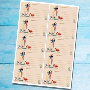 May include: Sheet of address labels featuring mermaid illustrations. Each label has a beige background with a mermaid design, including a blue-haired mermaid and a red-haired mermaid. The labels also include the text "Please Deliver To:" and lines for address information.