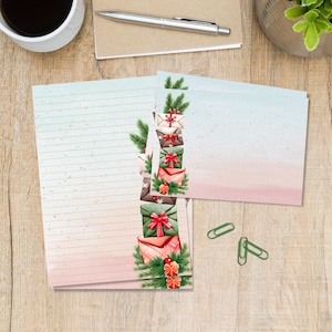 Op de afbeelding: Briefpapier set met gelijnd papier en blanco kaarten. De kaarten hebben een roze en blauwe aquarelverloop en een stapel geïllustreerde enveloppen met rode strikken en groene takjes. Inclusief groene paperclips.
