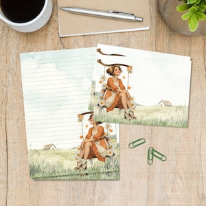 May include: Stationery set featuring a watercolour illustration of a person sitting on a swing in a field with daisies. The design includes a lined sheet and a matching card, both depicting a rural landscape with a small house in the distance.