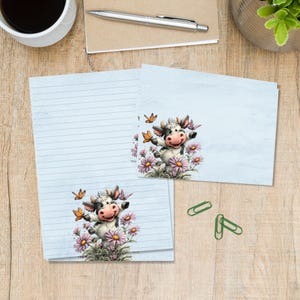 Pode incluir: Conjunto de papelaria com uma vaca de desenho animado rodeada por flores cor-de-rosa e borboletas. A vaca tem um padrão preto e branco com um nariz rosa e está sorrindo. O conjunto inclui papel pautado e cartões em branco, perfeito para escrever cartas ou notas.