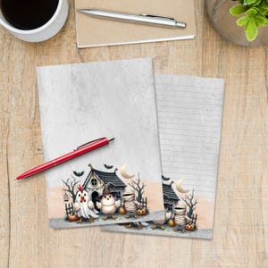 May include: Two sheets of stationery paper featuring a Halloween illustration at the bottom. The design includes a haunted house, a crescent moon, bats, and three characters: a chicken in a ghost costume, a chick in a witch hat, and a mummy chick.