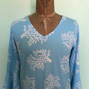 May include: A light blue blouse with a white coral print. The blouse has a v-neck and 3/4 sleeves.