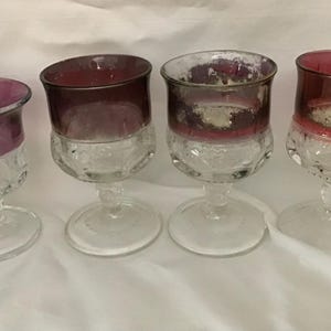 May include: Four vintage wine glasses with clear stems and bases. The upper portion of each glass is a deep red or purple color. The glasses have a decorative, textured pattern on the lower portion of the bowl.