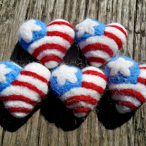 May include: Five felt heart-shaped decorations decorated with red, white and blue stripes and a white star. The decorations are reminiscent of the American flag.