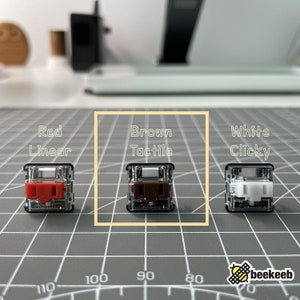 以下が含まれることがあります： 3つのメカニカルキーボードスイッチ。それぞれ色が異なり、感触も異なります。左側のスイッチは赤色でリニア、中央のスイッチは茶色でタクタイル、右側のスイッチは白色でクリックです。