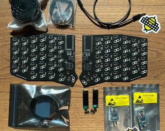 May include: A black and white keyboard kit with a bee logo. The kit includes two circuit boards, a cable, a set of keycaps, and a set of switches. The kit is packaged in a clear plastic bag.