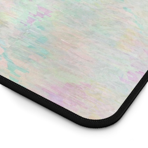 May include: A rectangular mouse pad with a pastel watercolor design in shades of pink, blue, and yellow. The edges are finished with a black stitched border. The design has a soft, blended appearance.