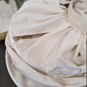 May include: A white cotton fabric bag with a drawstring closure. The bag is folded and has a white fabric lining.