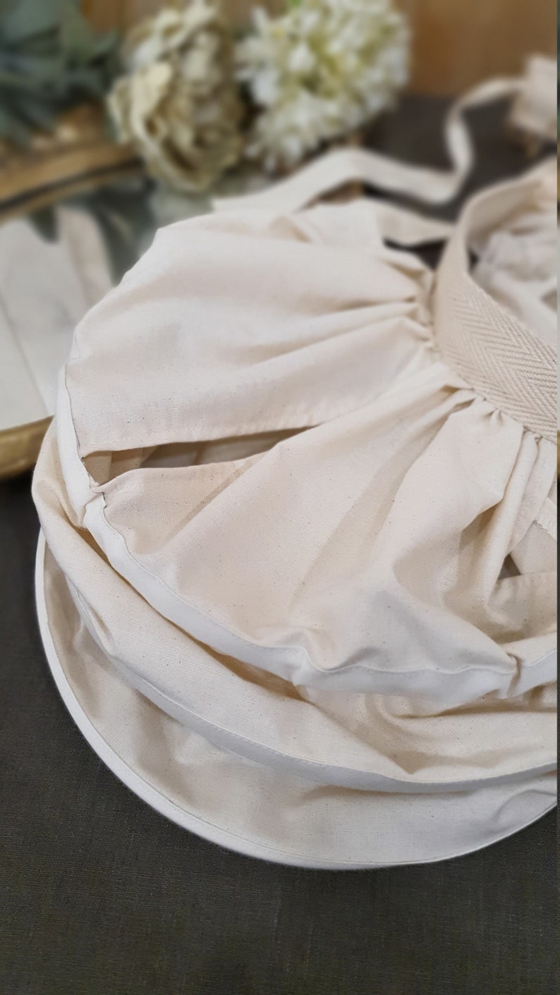 May include: A white cotton fabric bag with a drawstring closure. The bag is folded and has a white fabric lining.