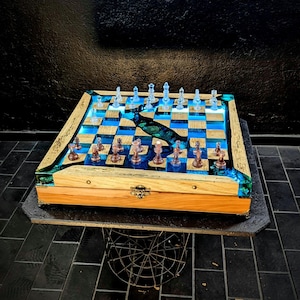May include: A handcrafted wooden chess set with a blue and gold resin inlay. The chessboard features a unique design with clear and brown chess pieces. The set is displayed on a dark surface, showcasing the intricate details of the game.