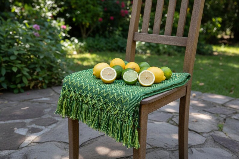 Puede incluir: Una silla de madera con una manta verde estampada y una colecci&oacute;n de limones y limas. La manta tiene un dise&ntilde;o en zigzag y flecos. Algunas de las frutas c&iacute;tricas est&aacute;n cortadas por la mitad. La escena est&aacute; ambientada al aire libre en un patio de piedra.