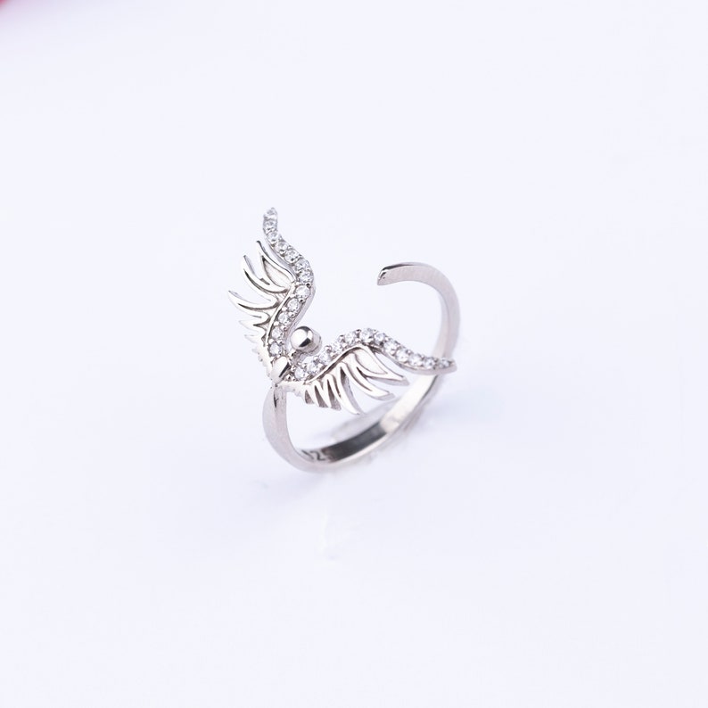 May include: A silver ring with a wing design, adorned with sparkling clear stones.