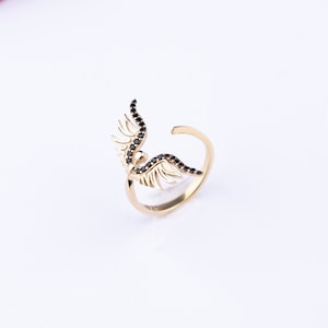 May include: Gold ring with black gemstone wings. The wings are detailed and have a delicate design.