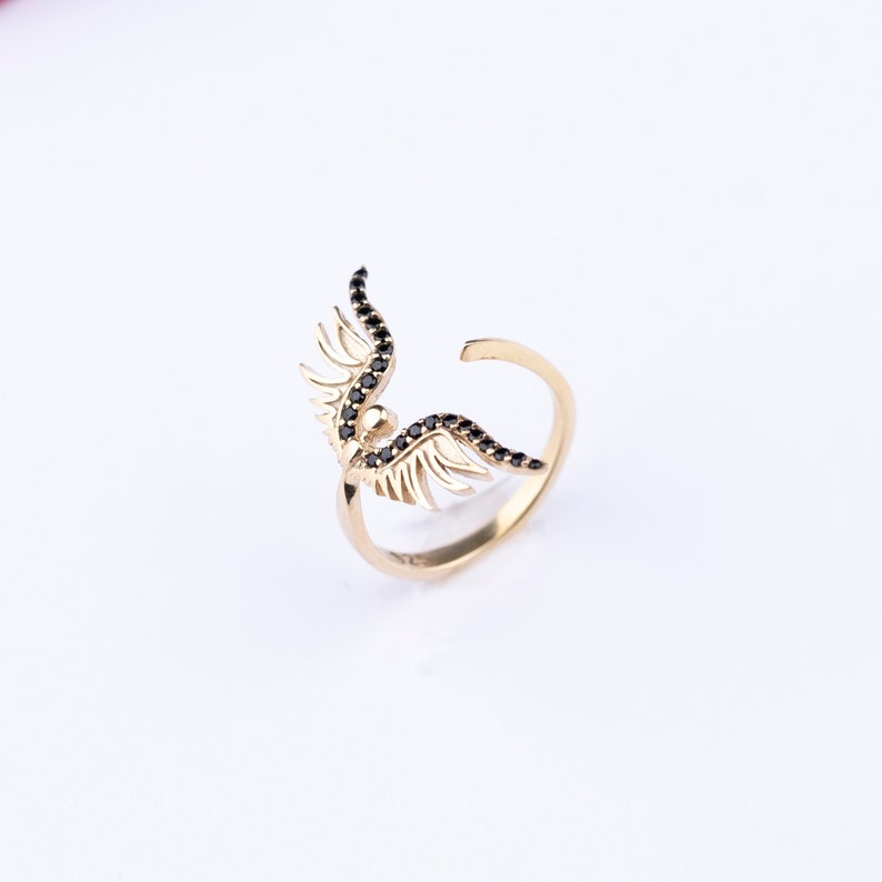 May include: Gold ring with black gemstone wings. The wings are detailed and have a delicate design.