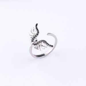 May include: A silver ring with black crystal wings. The wings are detailed and intricate, with a delicate design.