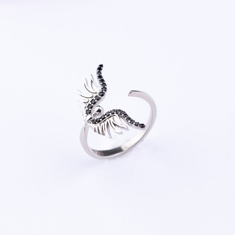 May include: A silver ring with black crystal wings. The wings are detailed and intricate, with a delicate design.