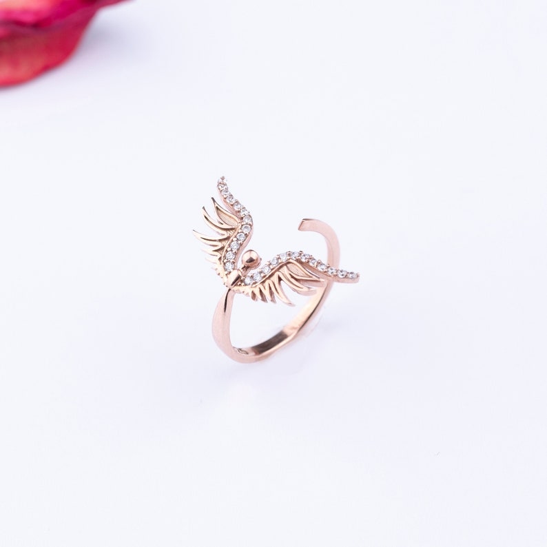 May include: A rose gold ring with a delicate angel wing design, adorned with sparkling clear stones.