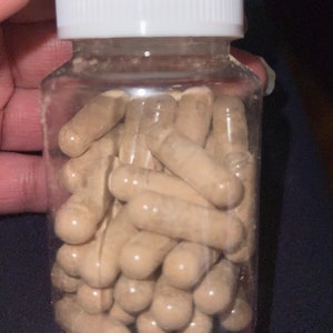 May include: A clear plastic bottle filled with a large quantity of brown capsules. The bottle has a white lid.