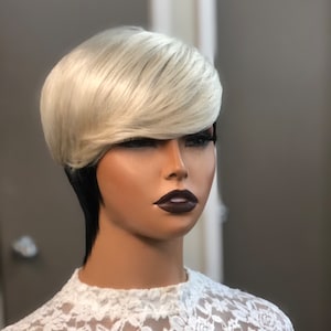 May include: A short blonde wig with a black under layer. The wig is styled with a side part and a fringe.