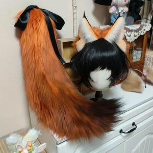 Puede incluir: Un conjunto de cola y orejas de zorro para cosplay. La cola es larga, esponjosa y naranja con una cinta negra. Las orejas son naranjas y blancas con puntas negras, unidas a una peluca con pelo negro. Un divertido accesorio de disfraz.