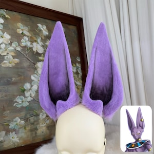 May include: A pair of tall, pointed, faux fur animal ears in a vibrant purple hue. The ears feature a dark, blackish-purple gradient at the base and inner sections, mimicking the appearance of the character Beerus from Dragon Ball Super.