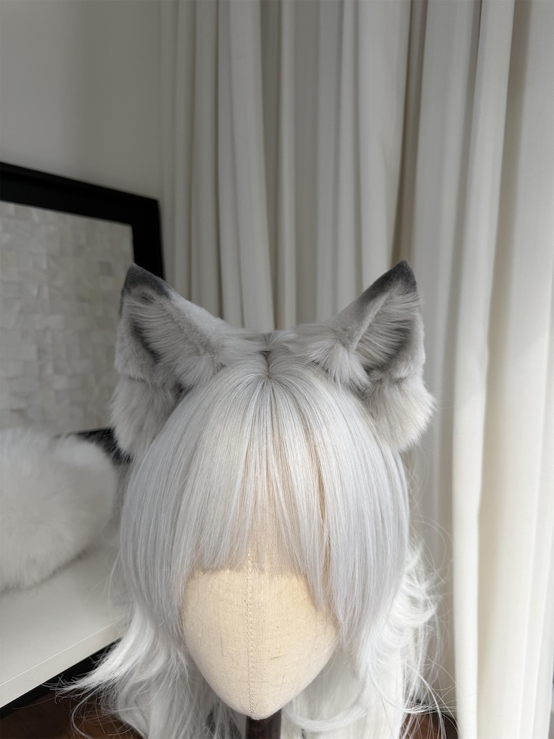 Puede incluir: Un accesorio de cosplay con una peluca de pelo largo plateado y un par de orejas de lobo grises y blancas. Las orejas son esponjosas y detalladas, con puntas grises m&aacute;s oscuras. La peluca tiene flequillo.