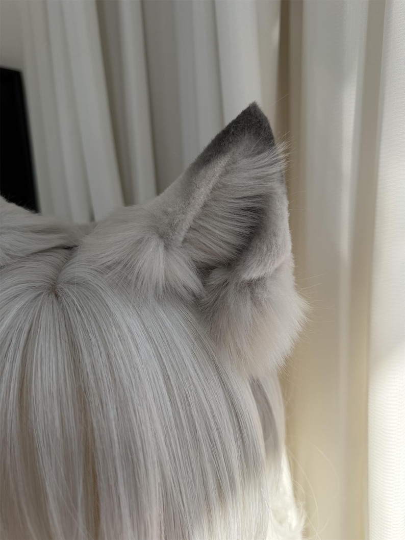 Puede incluir: Un par de orejas de lobo de piel sint&eacute;tica gris con puntas de color gris m&aacute;s oscuro. Las orejas est&aacute;n unidas a una peluca con pelo largo, liso y gris claro. Las orejas son esponjosas y detalladas, con un aspecto realista.