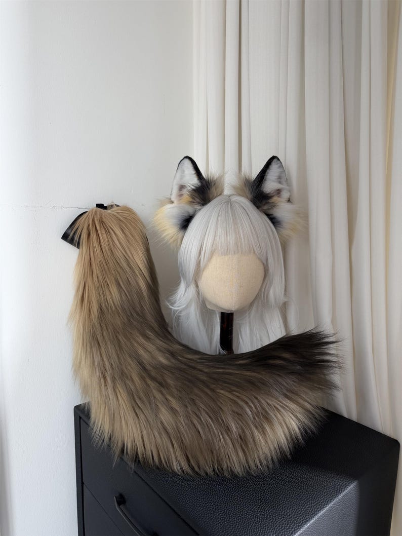 May include: A faux fur fox tail and ears set. The tail is a blend of brown and tan, with a black accent. The ears are white, tan, and black. The set is designed for cosplay or costume use.