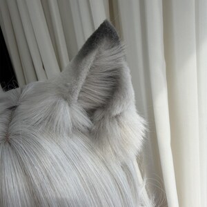 Puede incluir: Un par de orejas de lobo de piel sint&eacute;tica gris y blanca unidas a una peluca. Las orejas son de color gris claro con puntas grises m&aacute;s oscuras. La peluca tiene pelo largo, liso y gris claro.
